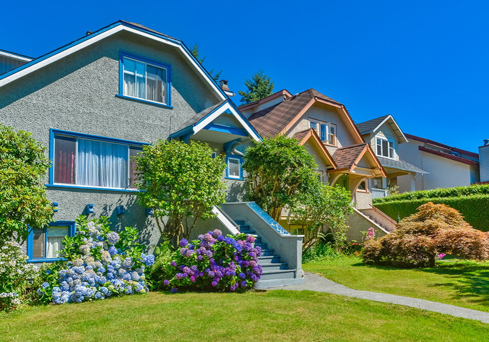 Snug warm family houses side by side. Residential house with the pathway over front yard lawn on blue sky background.